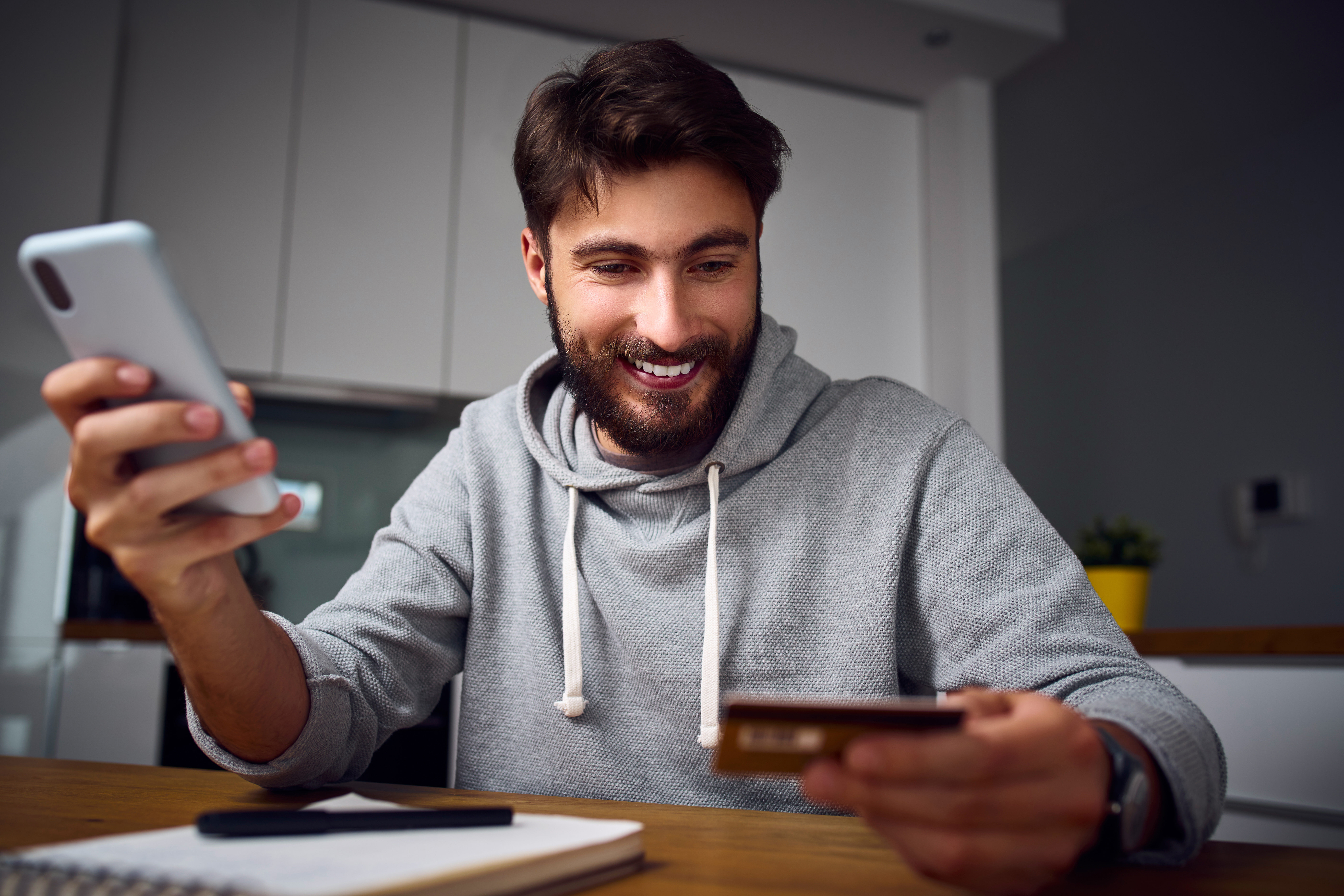 Happy young man making payments from home online with smartphone and credit card